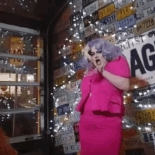 a woman in a pink dress stands in front of a wall of license plates including one that says ag