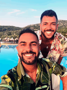 two men posing for a picture in front of a blue pool