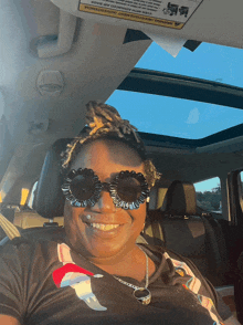 a woman wearing sunglasses sits in a car with a warning sign on the sunroof