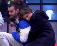 a man in a blue jacket is hugging another man