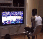 a man sits in a chair watching a basketball game on a flat screen tv