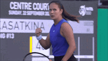 a woman in a blue tank top is holding a tennis racquet in front of a sign that says centre court