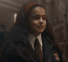a girl wearing a headband and a tie with a crest on her chest
