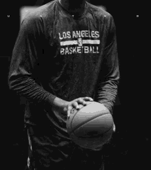 kobe bryant is wearing a los angeles basketball shirt and holding a basketball in a black and white photo .