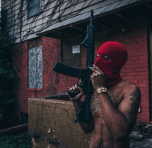 a shirtless man wearing a red mask is holding a gun in front of a brick building .