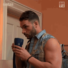 a man in a plaid shirt is drinking from a blue mug