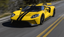 a yellow sports car with black stripes on the side is driving down a road