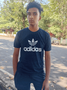 a young man wearing an adidas t-shirt stands in front of a street