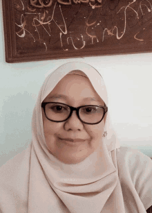 a woman wearing glasses and a hijab is smiling in front of a wall with writing on it