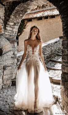 a woman in a wedding dress is standing in front of a stone wall