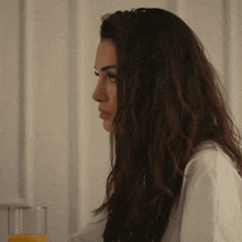 a woman in a white shirt sits at a table with a glass of orange juice in front of her