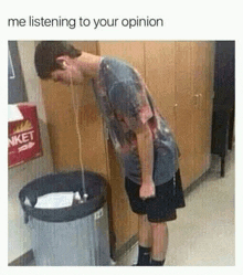 a man wearing headphones is standing next to a trash can and drinking out of it .