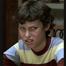 a young boy is making a funny face and wearing a striped shirt .