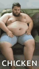 a fat man with a beard is sitting on a couch with his hands on his belly .