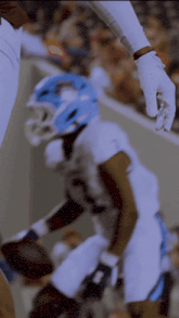 a football player wearing a blue helmet and white gloves holds the hand of another player