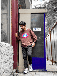 a man leaning against a wall with a pay24 sign on it