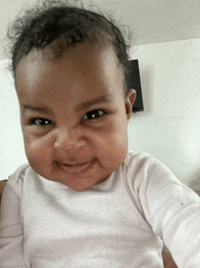 a baby with curly hair and a white shirt is smiling