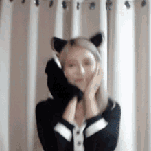 a woman wearing a cat ear headband is standing in front of white curtains .