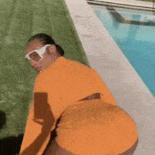 a man wearing sunglasses and an orange shirt is standing next to a swimming pool .