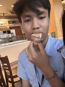 a man in a blue shirt with a lanyard around his neck is eating a doughnut