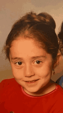 a young girl wearing a red shirt and earrings smiles at the camera