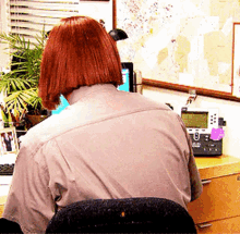 a woman with red hair is sitting at a desk with a phone and a map on the wall behind her