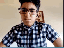 a young man wearing glasses and a plaid shirt looks at the camera