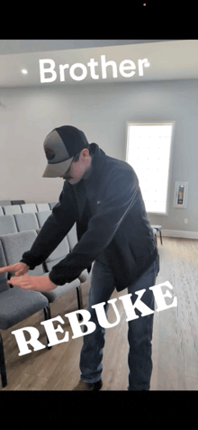 a man wearing a hat and a black jacket is standing in a room with the words brother rebuke behind him