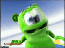 a green gummy bear is smiling and looking at the camera with a blue sky in the background .