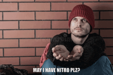 a man in a red hat is sitting in front of a brick wall with his hands out asking for money