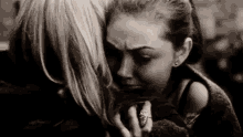 a black and white photo of two women hugging each other . one of the women is crying .