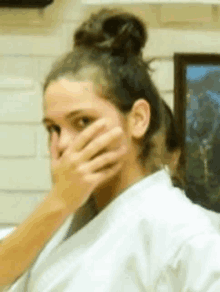 a woman in a karate uniform is covering her mouth with her hand .