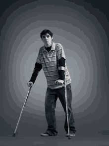 a young man with crutches is wearing a grey striped shirt