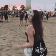 a woman is dancing in the dirt at a music festival while wearing a black bag with the word mile written on it .