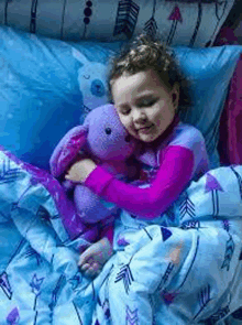 a little girl is sleeping in bed with a purple teddy bear .