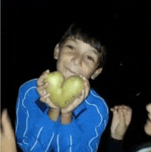 a young boy in a blue sweater is holding a heart shaped potato in his hands .