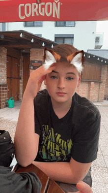 a boy wearing a corgon t-shirt is sitting at a table