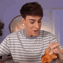 a young man wearing a striped shirt and a chain necklace is eating a slice of pizza .