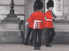 a group of soldiers in red uniforms are standing in front of a building and one of them has the word army on his belt