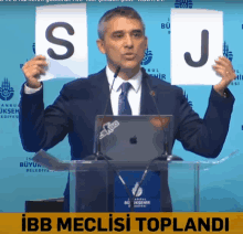 a man in a suit and tie holds up a sign with the letter s and j on it