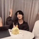 a man is sitting at a table with a cake on it and raising his hand in the air .