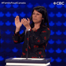 a woman applauds while standing at a podium in front of a microphone with the words family feud canada above her