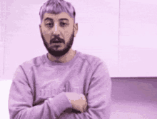 a man with purple hair and a beard is standing with his arms crossed and looking at the camera .