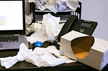 a box of tissues sits on a messy desk next to a laptop