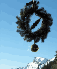 a christmas wreath with a gold ornament hanging from it in front of a snowy mountain