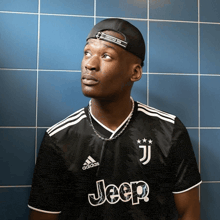 a man wearing a black jeep shirt stands in front of a blue wall