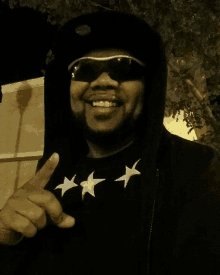 a man wearing sunglasses and a black hoodie has three white stars on his shirt