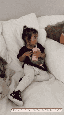 a little girl is sitting on a bed drinking from a pink cup with the caption when did she grow up