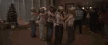 a group of young women are dancing together in a room with a christmas tree in the background .