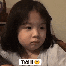 a little girl with short hair is making a funny face and the word triiiii is on the bottom of the picture .